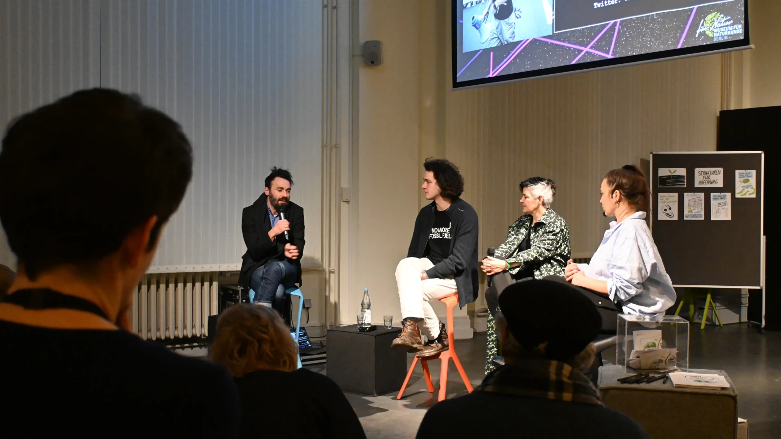 Vier Menschen sitzen auf Stühlen und diskutieren miteinander.